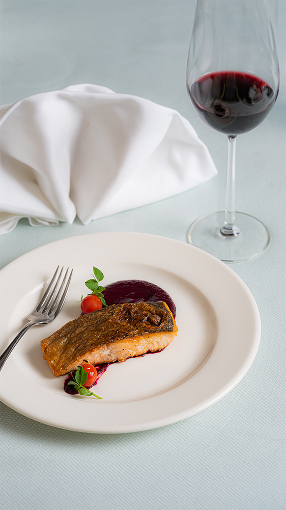 Fine dining salmon dish with beetroot puree and cherry tomatoes plated elegantly with a glass of red wine restaurant food photography